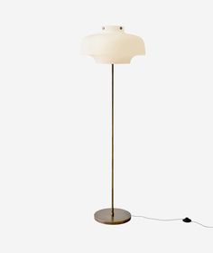 a floor lamp with a white shade on it's base and a black cord plugged in