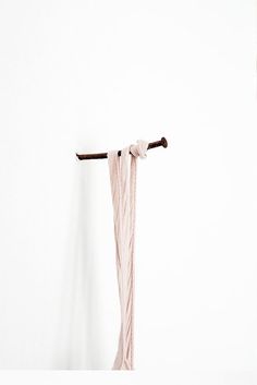 a piece of pink yarn hanging from a hook on a white wall with a wooden stick sticking out of it