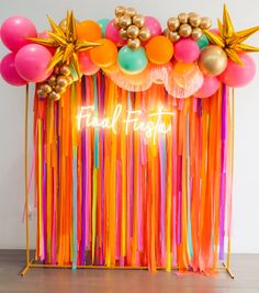 an orange, pink, and yellow backdrop with balloons and streamers that say final fiesta