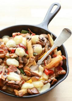 a skillet filled with pasta and vegetables on top of a wooden table next to a fork