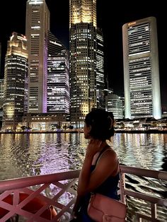 a woman sitting on the back of a boat in front of tall buildings at night