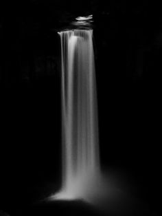 a black and white photo of a waterfall in the dark with light coming from it