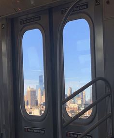 two windows on the side of a train with city buildings in the backround