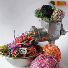 several balls of yarn are sitting in a bowl on a white surface and next to a spool of thread