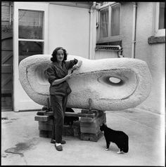 a woman standing next to a giant object with a cat on the ground in front of it