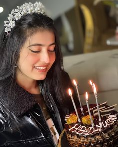 a woman is smiling while holding a cake with lit candles on it and wearing a tiara