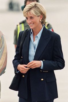 a woman in a blue shirt and black blazer smiles at the camera while standing next to other people