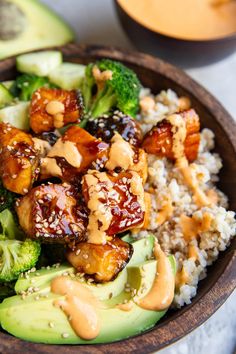 a wooden bowl filled with rice and broccoli covered in peanut sauce next to an avocado