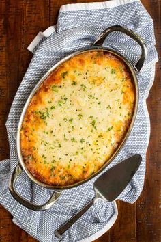 a casserole dish with cheese and herbs in it on a blue towel next to a spatula