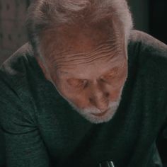 an older man holding a wine glass looking down at the ground with his hand on it