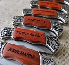 six knives with engraved names on them sitting on a tableclothed surface in rows