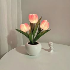 a white vase filled with pink flowers sitting on top of a table next to an open book