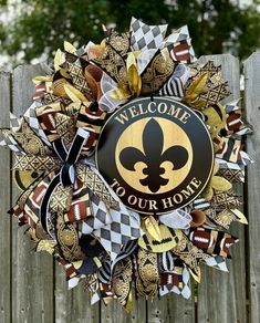 a welcome to our home wreath hanging on a wooden fence with the words welcome to your home in gold, black and white