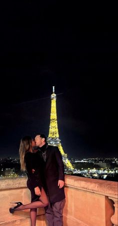 a man and woman kissing in front of the eiffel tower, at night