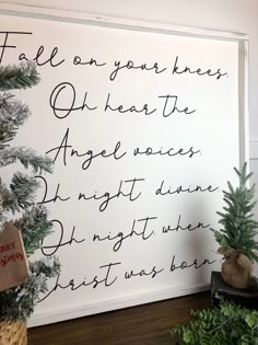 a white wall with writing on it next to christmas trees and potted planters