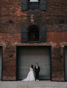 a bride and groom standing in front of an old brick building