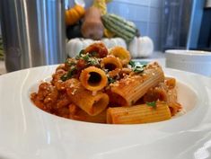 a white plate topped with pasta and meat covered in sauce next to a silver pot