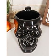 a black skull shaped vase sitting on top of a table next to an orange plant