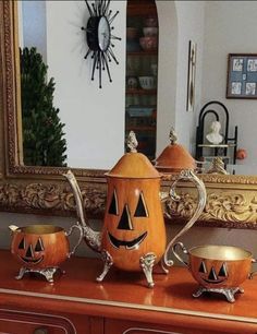 an orange tea pot with two pumpkin faces on it and three matching cups in front of a mirror