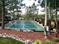 an outdoor tennis court surrounded by trees and rocks in the middle of a garden area