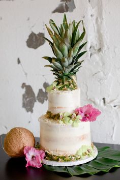 a three tiered cake with fresh flowers on the top and a pineapple next to it