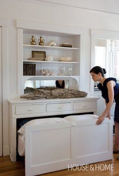 a woman standing in front of a white table with drawers and shelves on it,