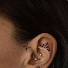 a woman's ear with small black dots and stars on her left behind the ear