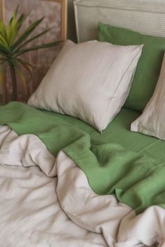 a bed with green sheets and two white pillows on top of it, next to a potted plant