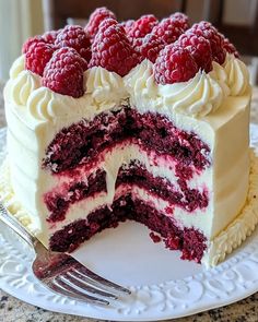 a cake with white frosting and raspberries on top is sitting on a plate