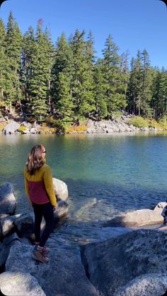 a woman standing on top of a rock next to a lake filled with rocks and trees