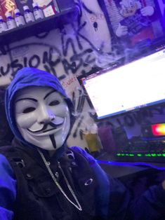 a person wearing a mask sitting in front of a computer screen with graffiti on it