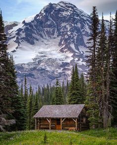 a cabin in the woods with mountains in the background and snow on the top of the mountain