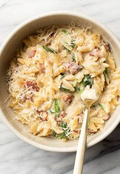 a white bowl filled with pasta and spinach on top of a marble countertop