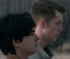 two young men standing next to each other in front of a forest with no leaves