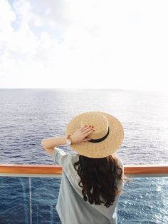 a woman wearing a straw hat looking out at the ocean from a cruise ship deck