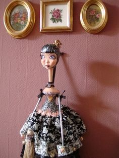 a doll is standing in front of a wall with two pictures on the wall behind it