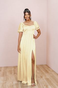 a woman standing in a room wearing a yellow dress with a slit down the side