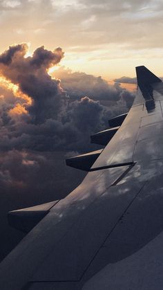 the wing of an airplane as it flies through the sky with clouds in the background