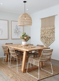 a dining room table with chairs and pictures on the wall behind it, along with hanging art