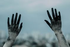 two hands with black and white gloves reaching up into the air to catch something in the sky