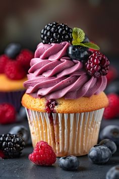 a cupcake with purple frosting and fresh berries on top, surrounded by raspberries