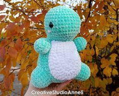 a small crocheted stuffed animal sitting in front of a tree with autumn leaves