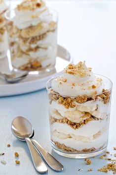 two desserts with banana slices and whipped cream in them on a white table next to silverware