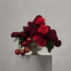 a vase filled with roses and apples sitting on top of a white table next to a gray wall