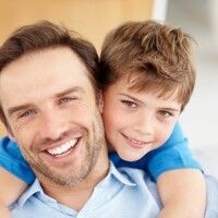 a man holding a little boy in his arms while he is smiling at the camera