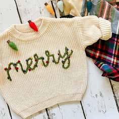 a sweater with the word merry written on it sitting next to other clothing and accessories