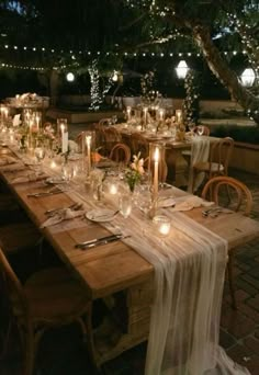 a long table with candles and flowers on it is set up for an outdoor dinner