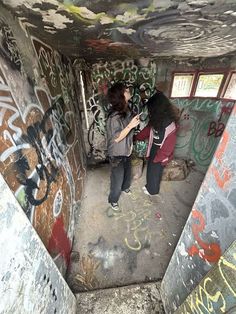 two people standing in an abandoned building with graffiti on the walls