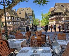 tables and chairs are set up outside in front of some old buildings with people walking by