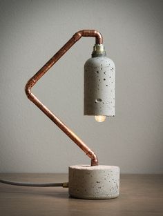 a table lamp made out of concrete and copper pipe with a light bulb on top